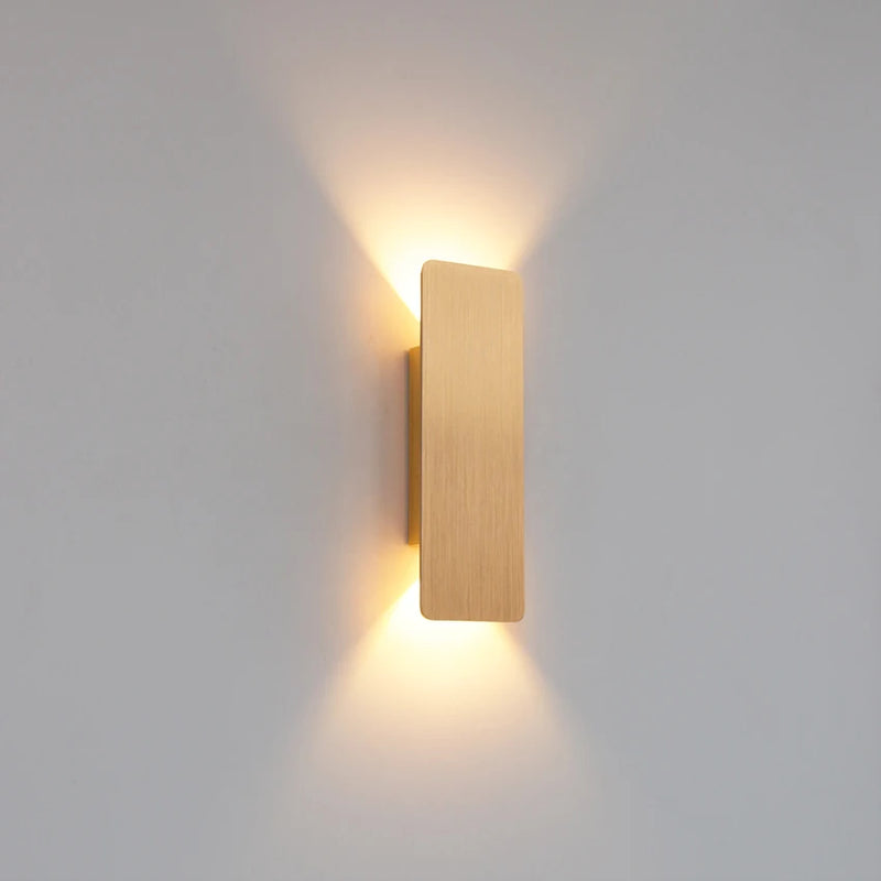 Arandela LED moderna dourada instalada na parede com iluminação bidirecional, ideal para salas, quartos e corredores sofisticados.