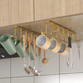 Suporte organizador suspenso dourado instalado sob o armário da cozinha, com ganchos para pendurar xícaras, canecas e utensílios.