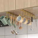 Suporte organizador suspenso dourado instalado sob o armário da cozinha, com ganchos para pendurar xícaras, canecas e utensílios.